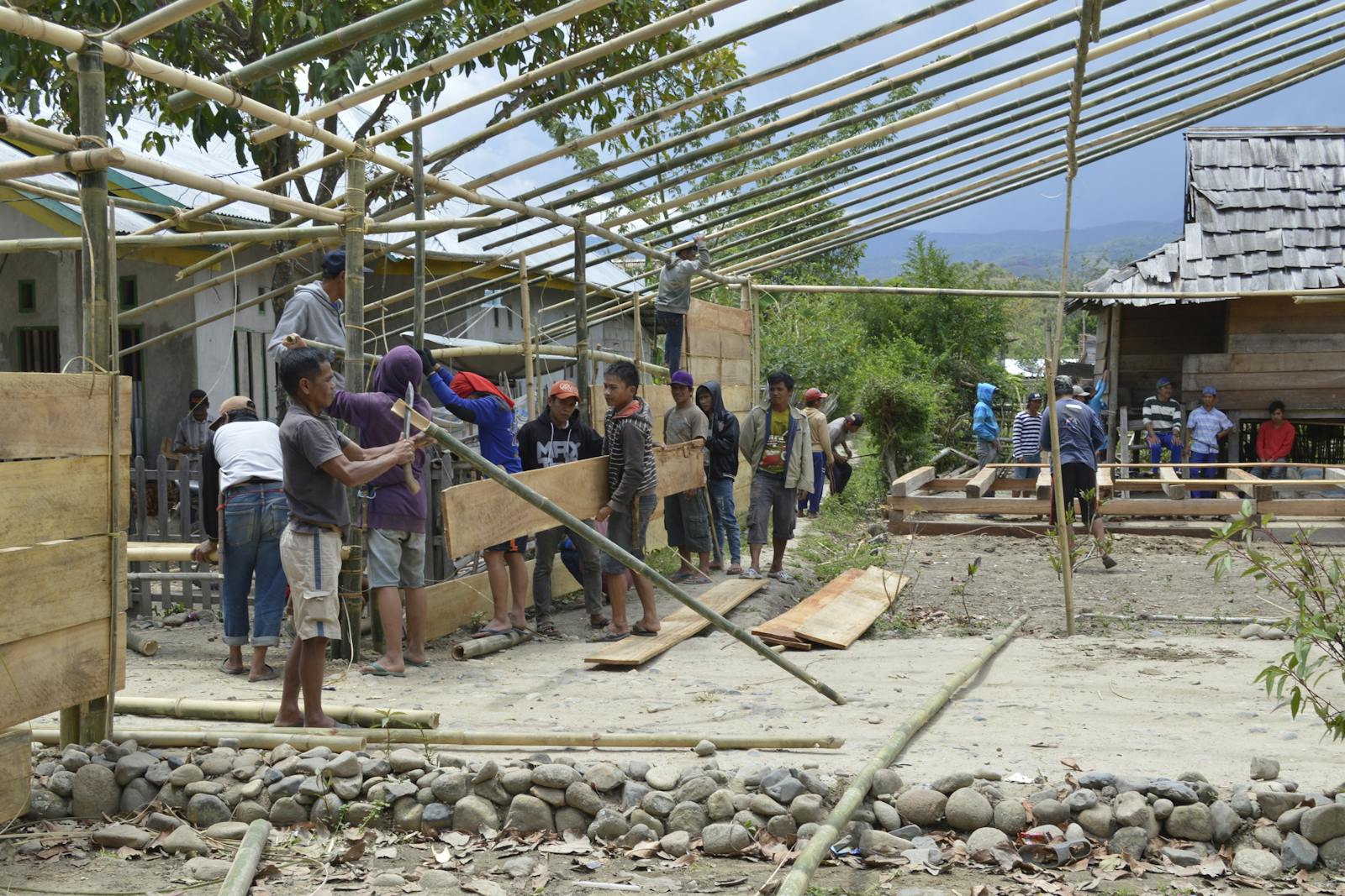 Community building a bamboo structure together with children watching